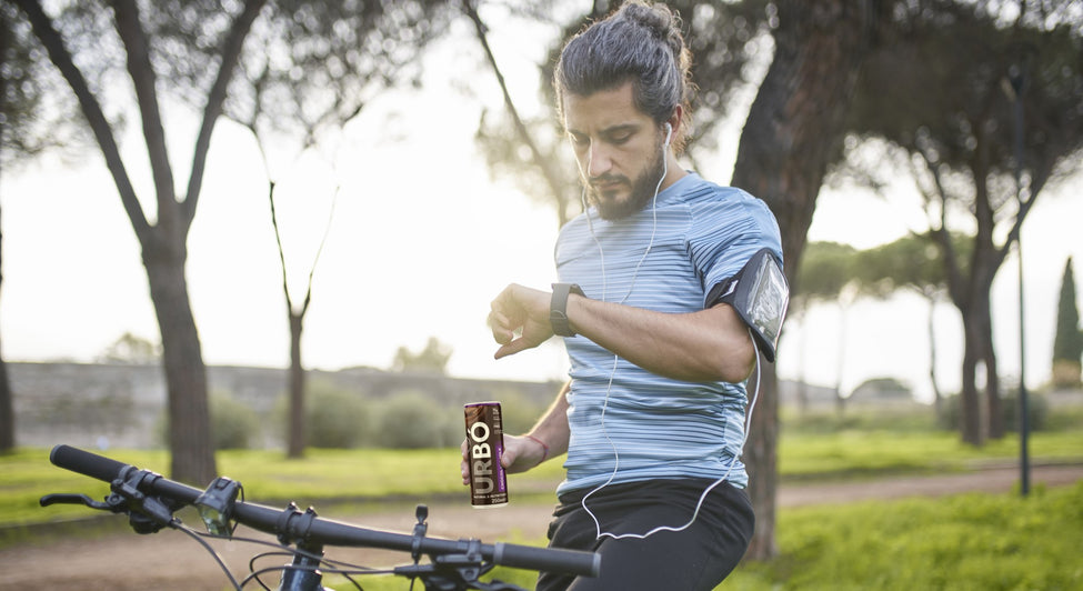 Cyclist checking smartwatch next to bike with a can of URBÓ protein milk in focus.